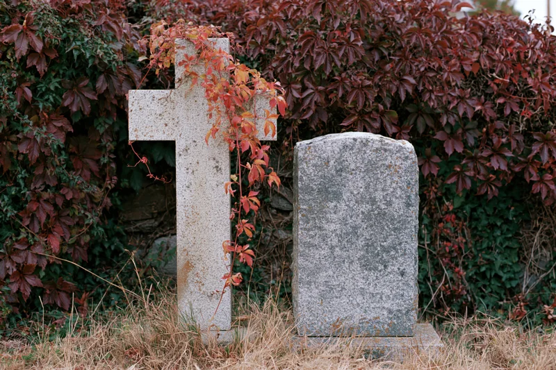 Two weathered granite grave markers in a small cemetery plot surrounded by autumn foliage