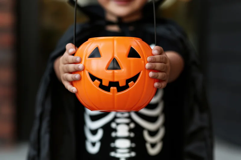 Child in skeleton costume holding orange pumpkin bucket for halloween trick or treat