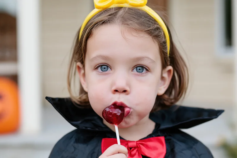 Young girl in vampire costume sucking red lollipop outdoors on halloween