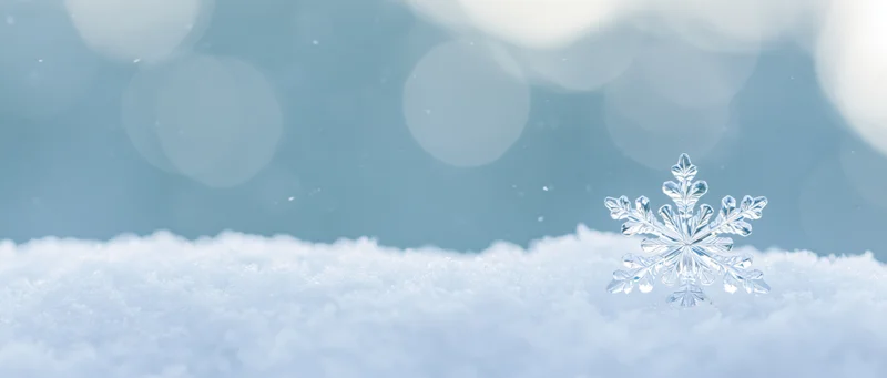 Crystal snowflake ornament resting on snow with bokeh background