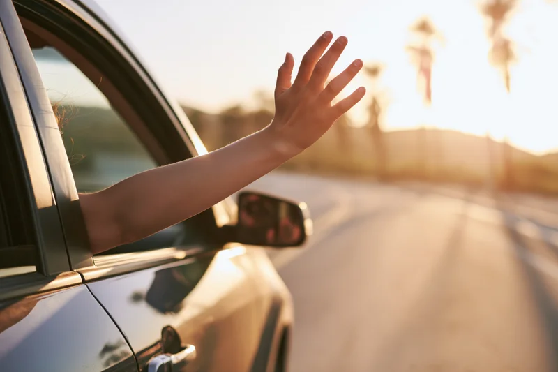 Woman’s arm and hand reaching out of moving car window on sunlit road
