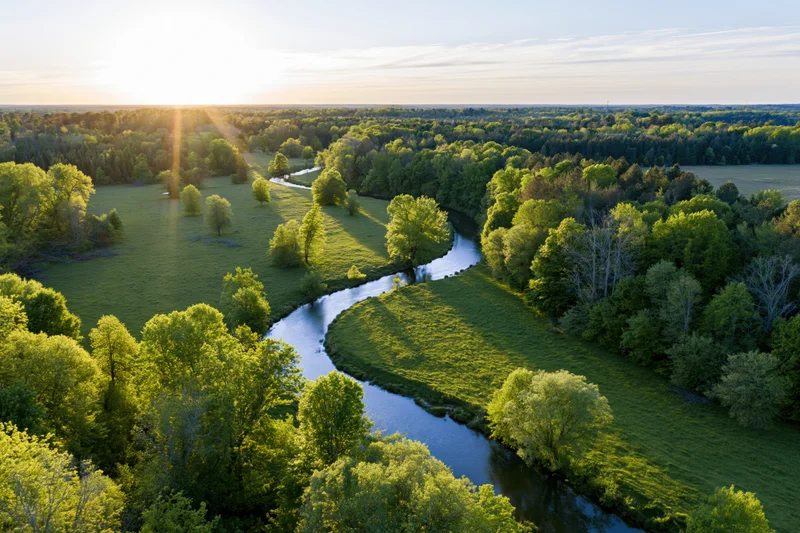 Aerial view of a winding river flowing through green forests and meadows at sunrise