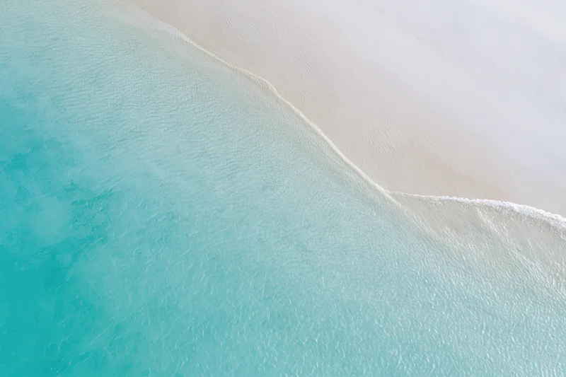 Aerial top-down view of turquoise ocean meeting white sandy beach at tropical shoreline
