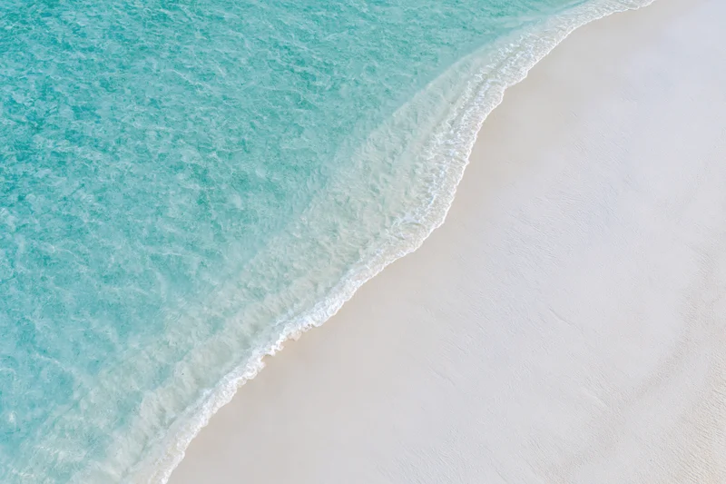 Aerial top-down view of turquoise ocean waves meeting white sandy beach