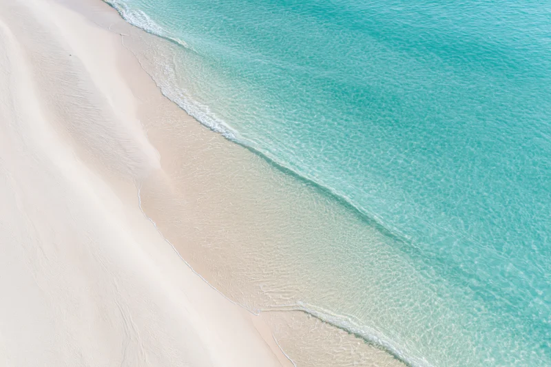 Aerial top-down view of a clear turquoise ocean meeting white sand beach