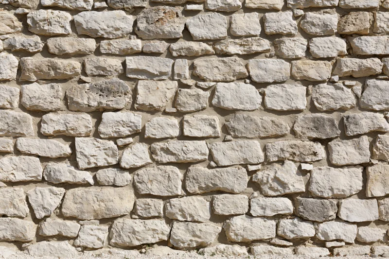 Ancient limestone rubble wall filling the frame with irregular stones and mortar under sunlight