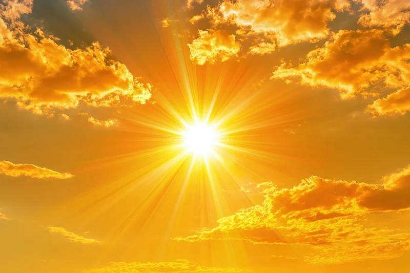 Blazing sun with starburst rays shining through orange clouds in the sky