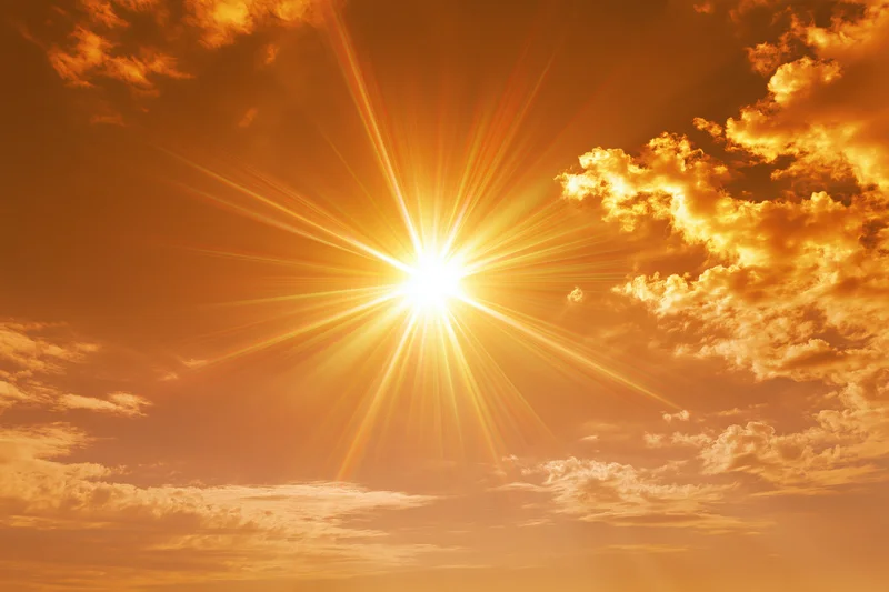 Blazing sun with starburst rays shining through orange clouds in the sky
