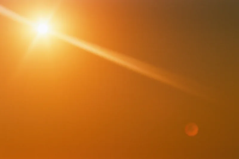 Blazing sun low in hazy summer sky with lens flare and warm orange glow