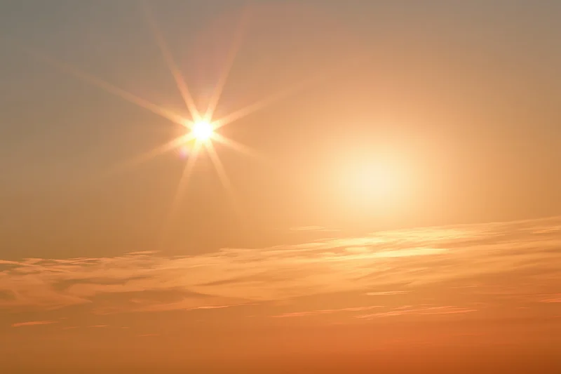 Blazing sun low in hazy summer sky with clouds and warm glow