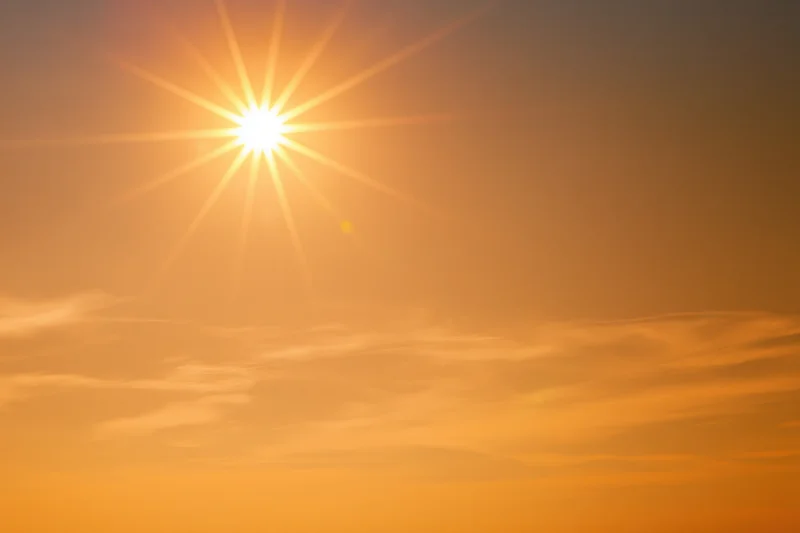 Blazing sun low in a hazy summer sky with wispy clouds and warm golden light