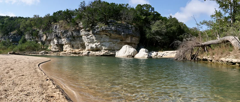 Clear shallow river with sandy gravel bank curving alongside rocky cliff under blue sky