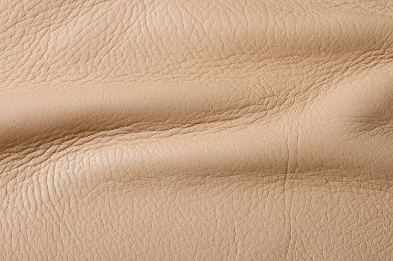 Close-up of aged beige leather surface with natural grain and folds