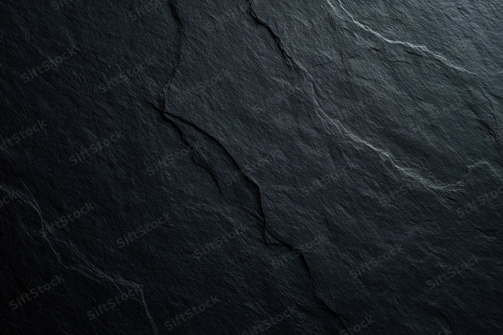 Close-up of dark slate rock surface with natural cracks and veins filling the frame