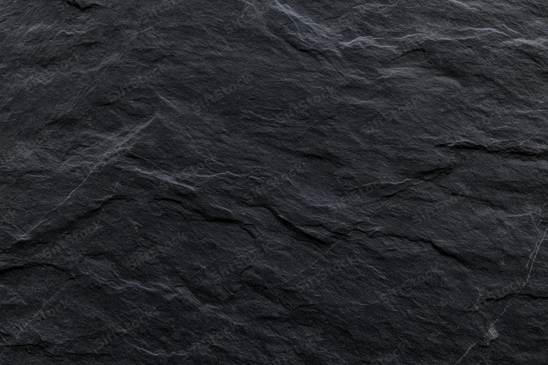 Close-up of dark slate stone surface with natural texture and cracks filling the frame