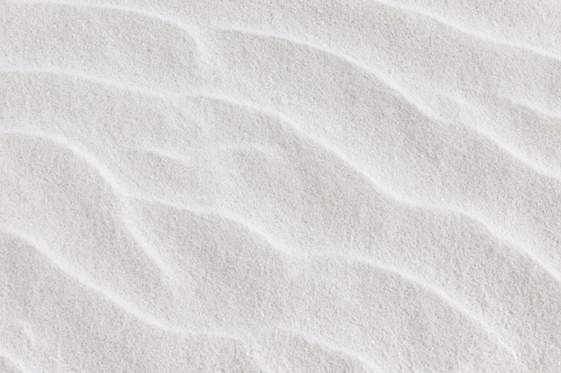 Close-up of fine white beach sand with rippled texture filling the frame