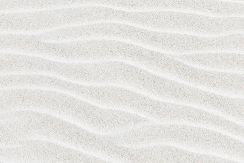 Close-up of fine white beach sand with natural ripples forming a smooth textured pattern