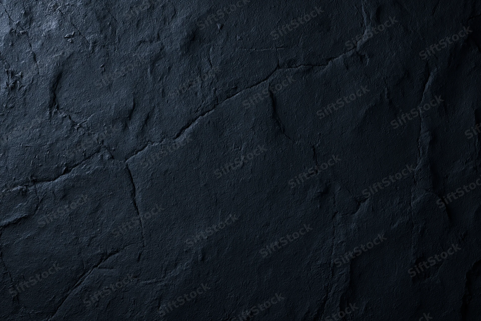Close-up of dark rough stone or plaster surface with cracks and texture