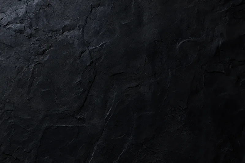 Close-up of dark rough stone or plaster surface with cracks and texture