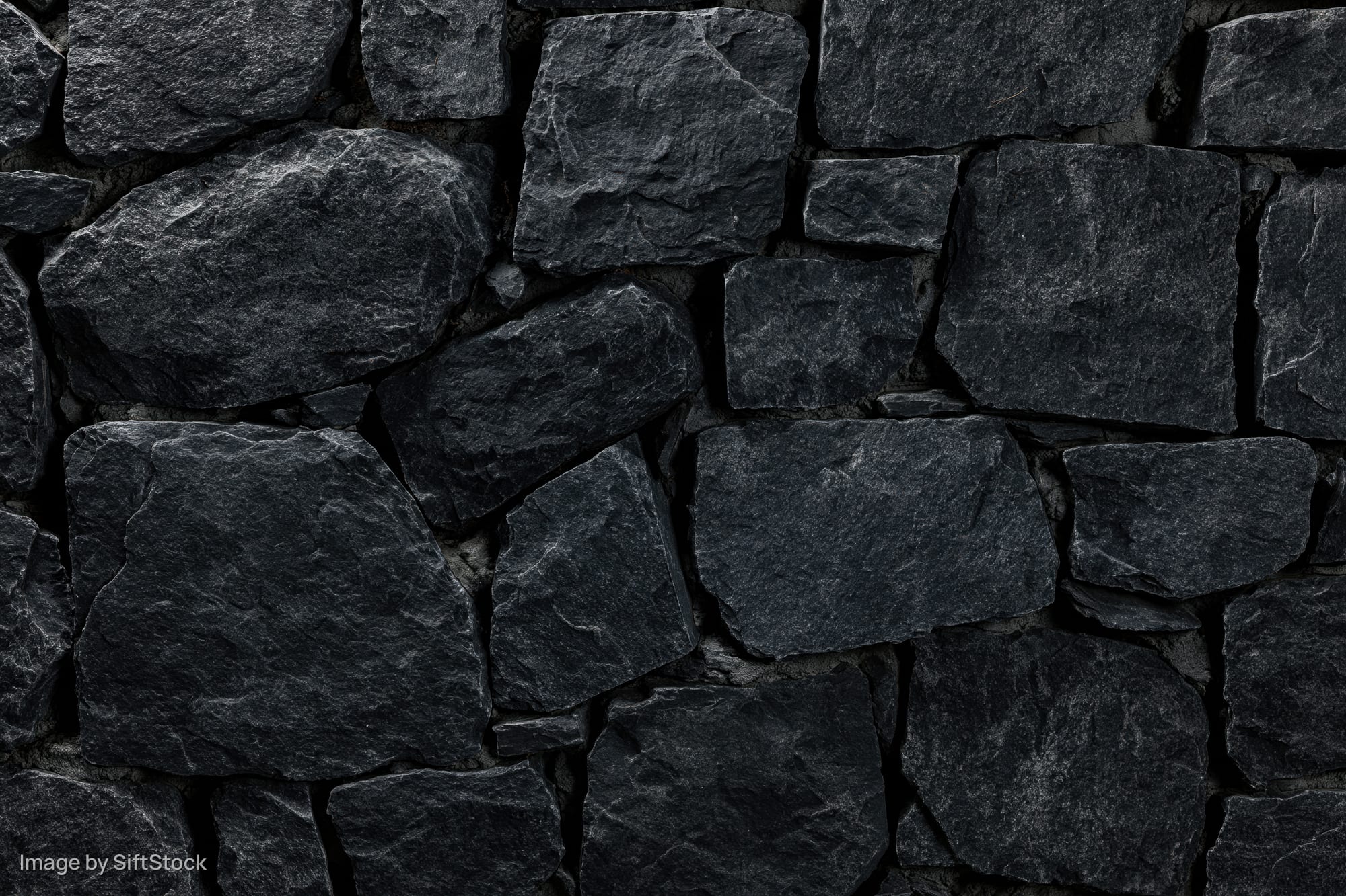 Close-up of dark slate stone wall with rough irregular texture