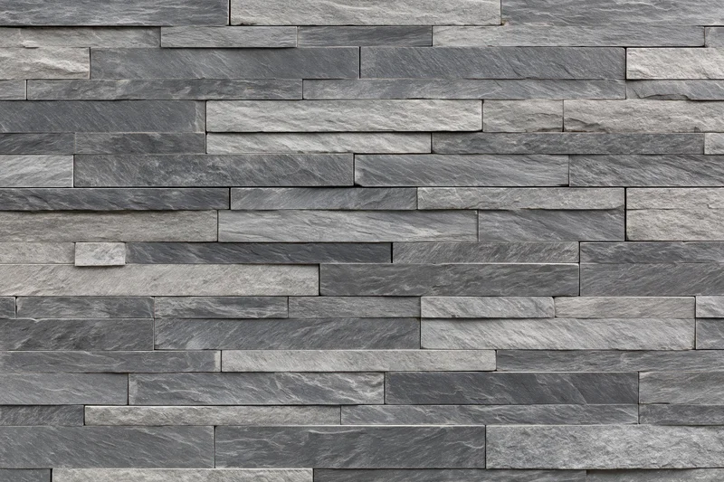 Stacked slate stone wall with horizontal rectangular tiles forming a textured gray facade