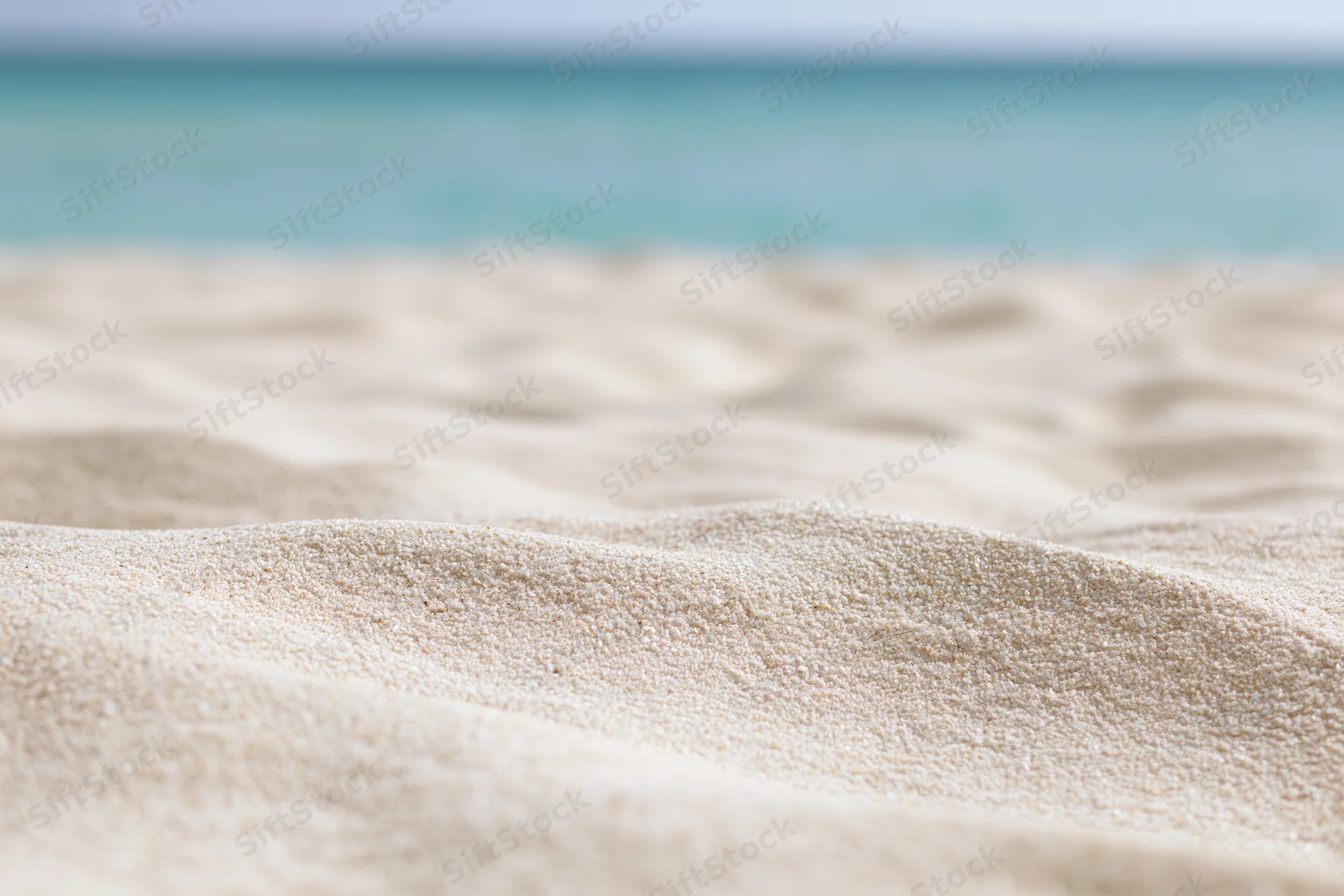 Closeup of pale white-gold beach sand with undulating texture and turquoise ocean in background