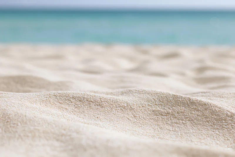 Closeup of pale white-gold beach sand with undulating texture and turquoise ocean in background