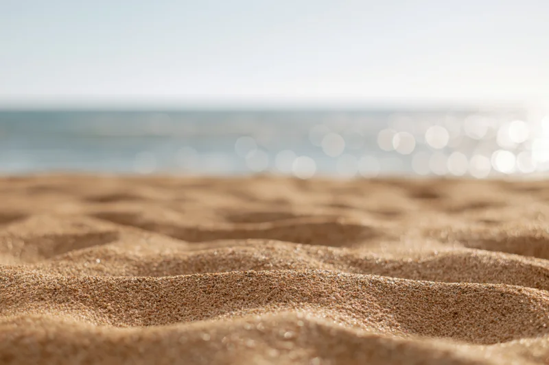 Close-up of rippled dry sand on a beach with ocean and sunlight in the background