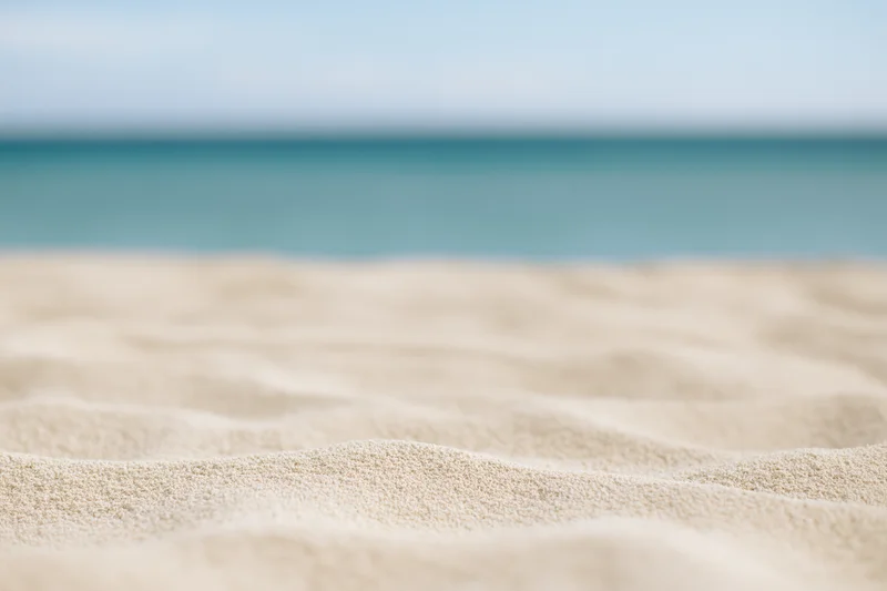 Close-up of pale dry beach sand with soft ripples and ocean in the background