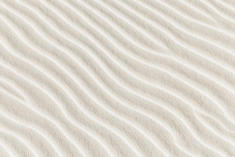 Close-up top-down view of white sand with wavy ripples across the surface