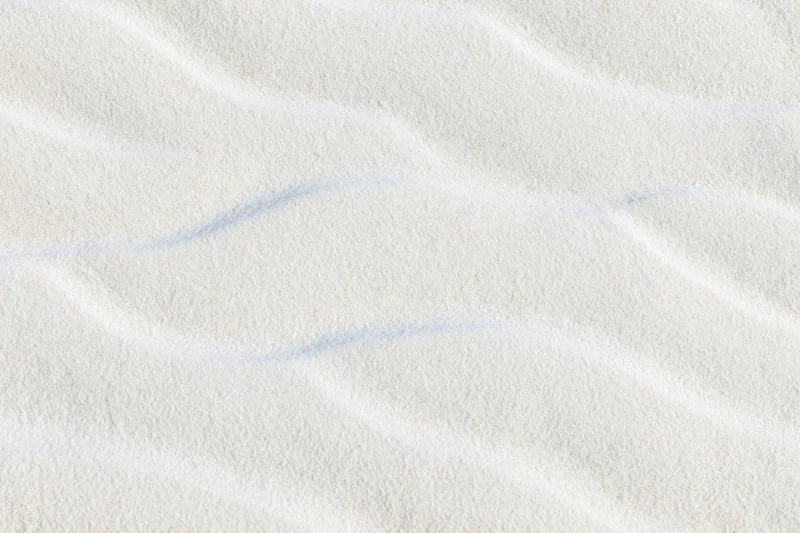 Close-up top-down view of fine white beach sand with rippled texture filling the frame