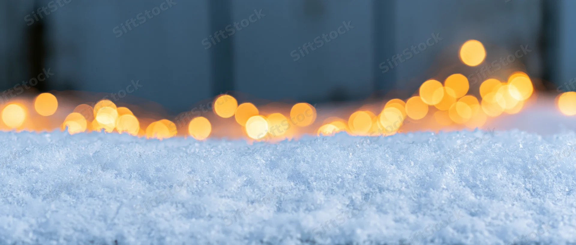 Close-up of fresh snow surface with blurred warm lights in the background at night