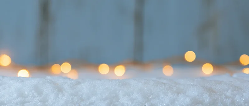 Close-up of fresh snow surface with blurred warm lights in the background