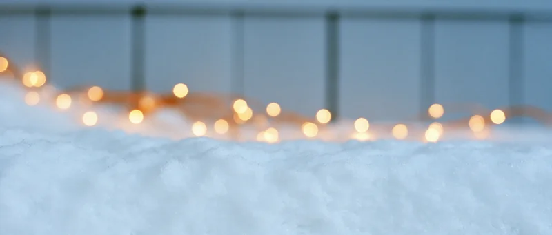 Fresh snow surface with blurred warm string lights in the background