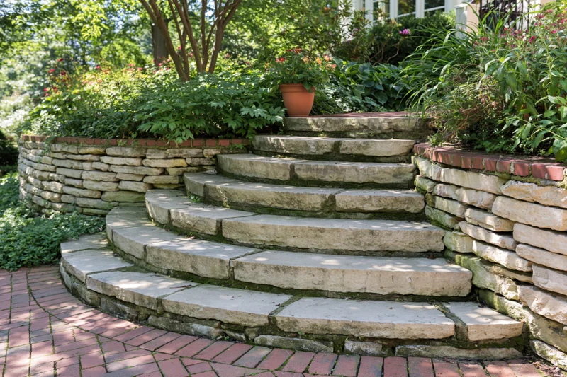 Curved stone staircase leading up through a lush garden bordered by retaining walls and greenery