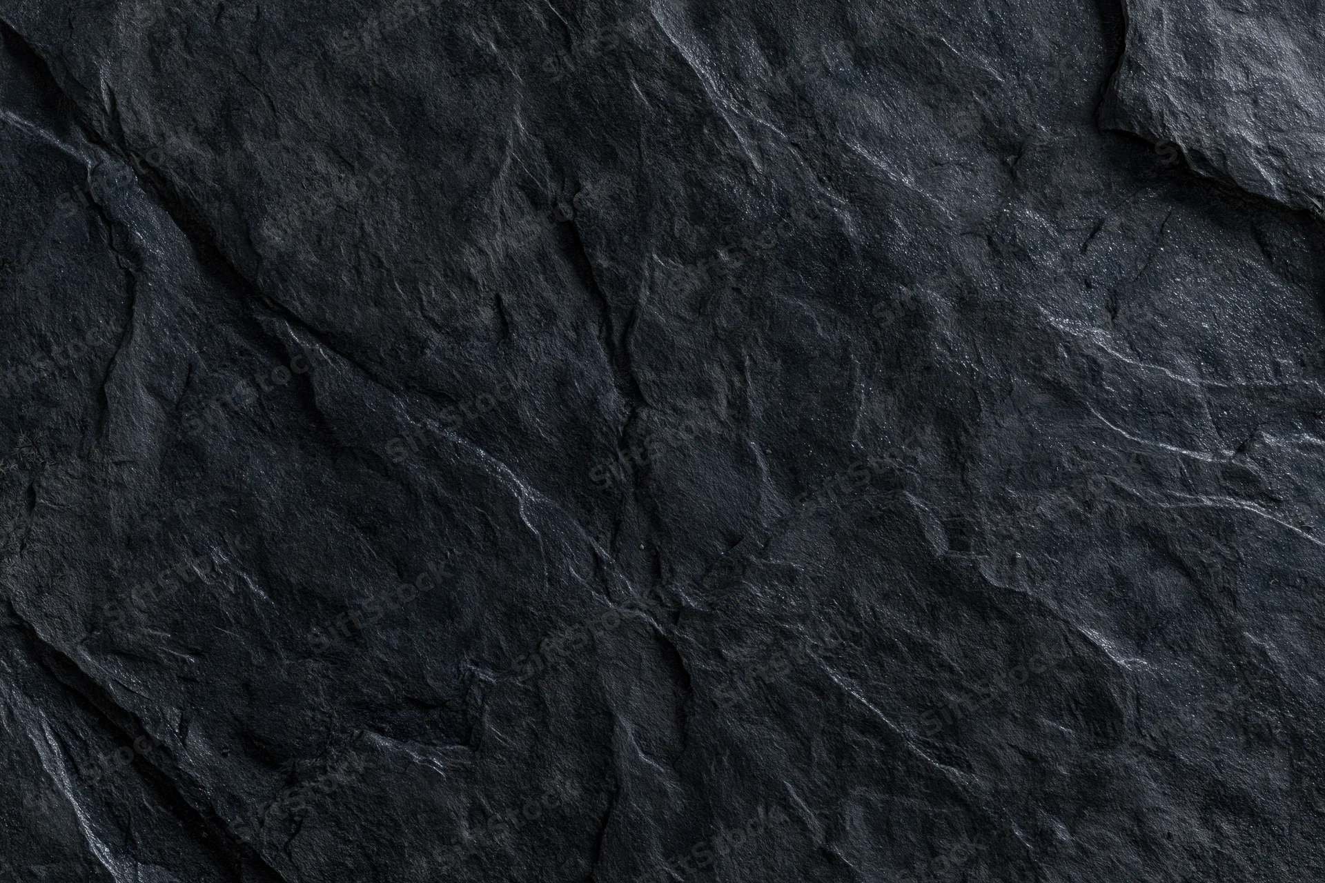 Dark rough slate rock surface filling the frame with natural texture and cracks