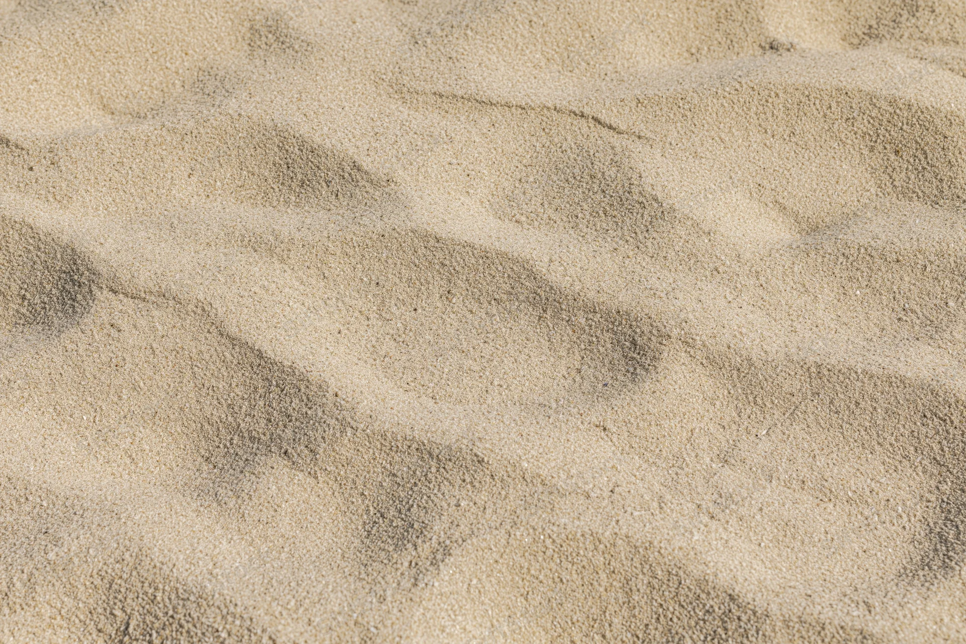 Closeup of dry beach sand surface with wind-formed ripples and undulations