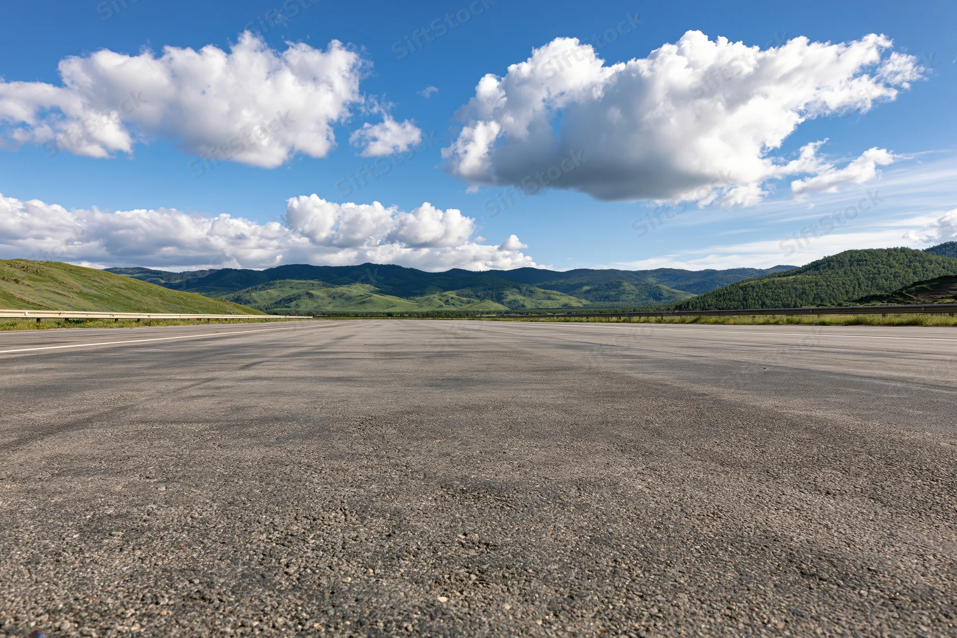 Empty asphalt highway stretching to the horizon with green hills and blue sky above