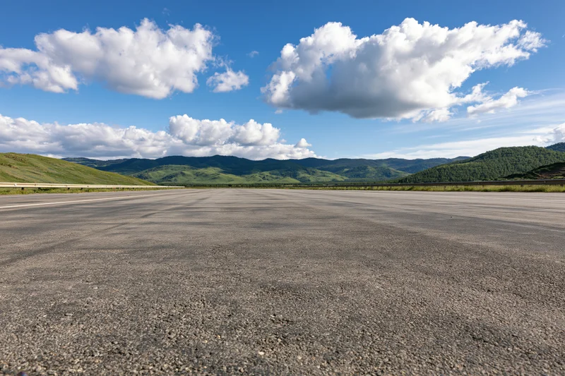 Empty asphalt highway stretching to the horizon with green hills and blue sky above