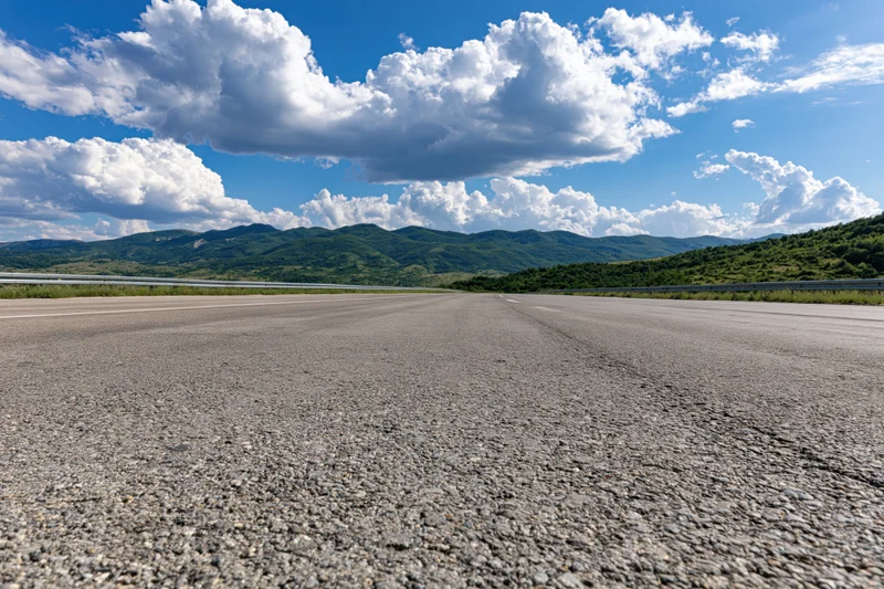 Empty asphalt highway stretching to the horizon with mountains and clouds above