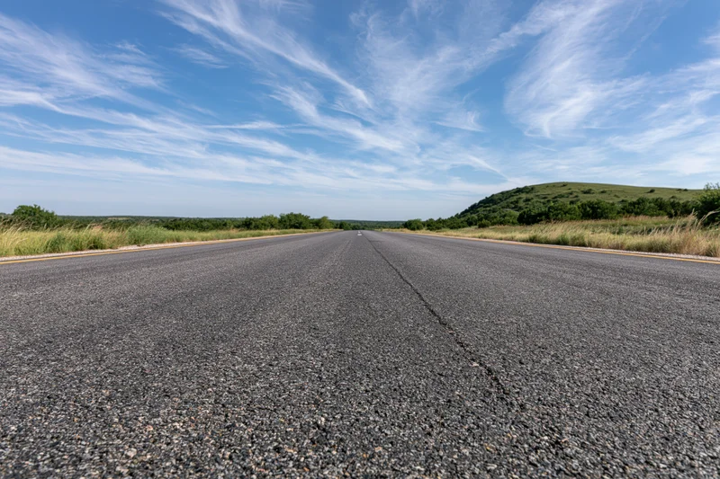 Empty asphalt highway stretching to the horizon under a blue sky with wispy clouds