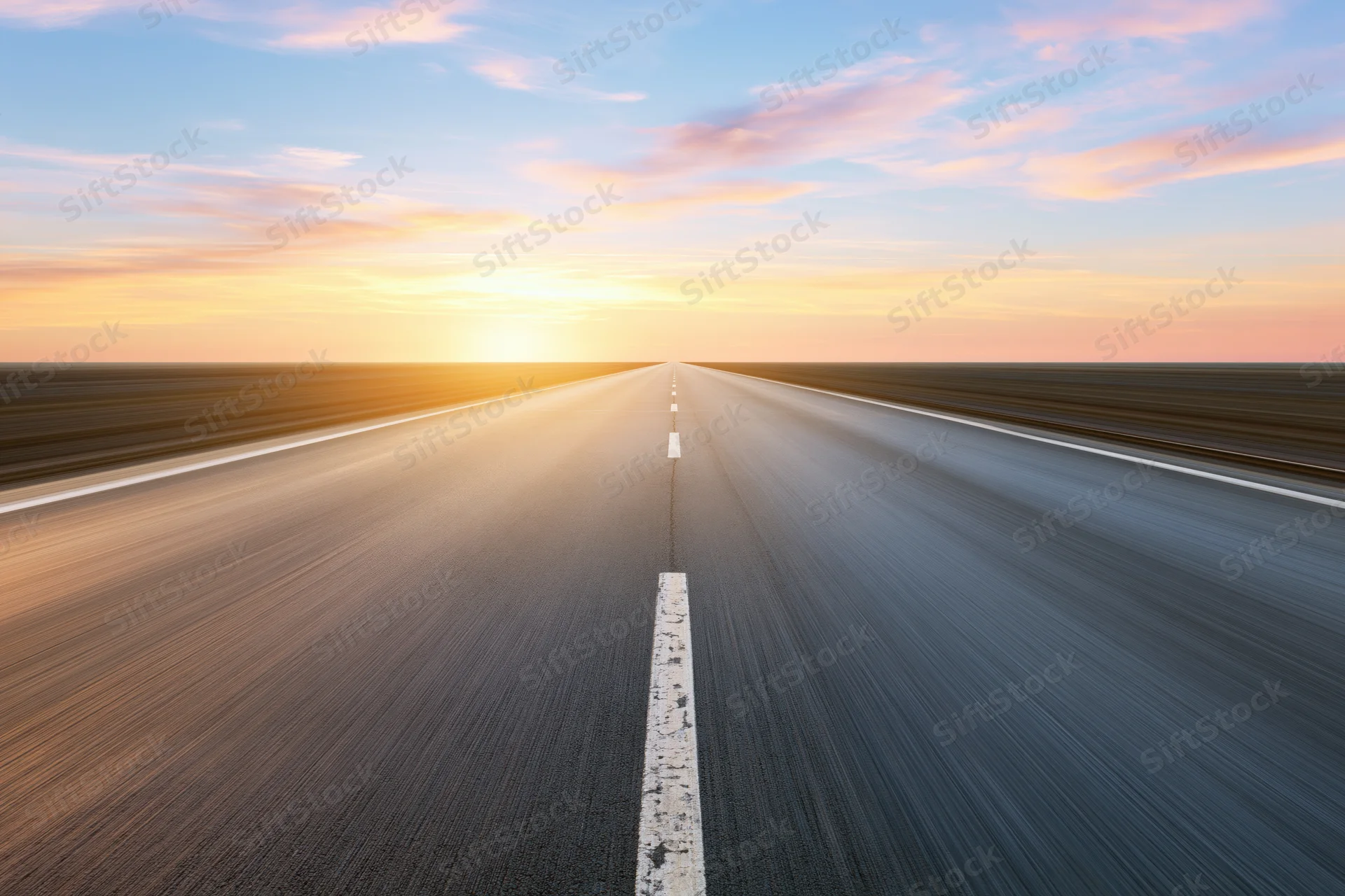 Straight asphalt highway stretching to the horizon at sunset with motion blur and white centerline