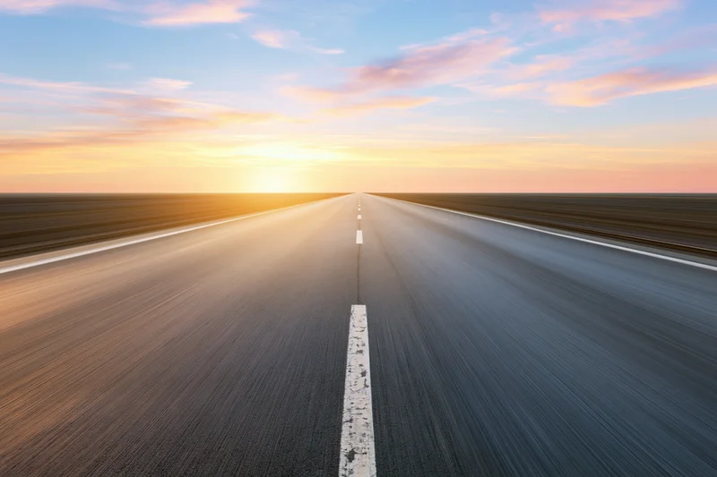 Straight asphalt highway stretching to the horizon at sunset with motion blur and white centerline