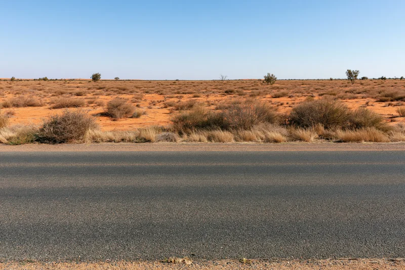 Empty asphalt road stretching across a flat arid desert landscape under a clear blue sky