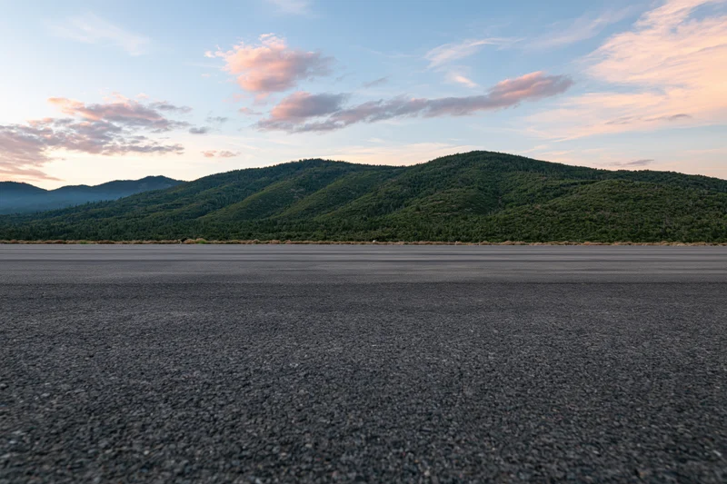 Empty asphalt tarmac stretching to distant forested mountains under soft twilight sky
