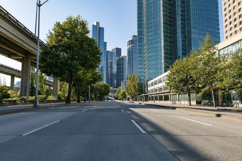 Empty multi-lane urban road stretching toward a cluster of modern glass skyscrapers under clear blue sky