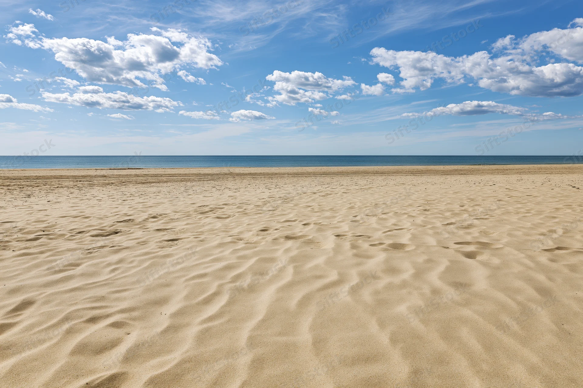 Empty sandy beach stretching toward calm ocean under blue sky with scattered clouds