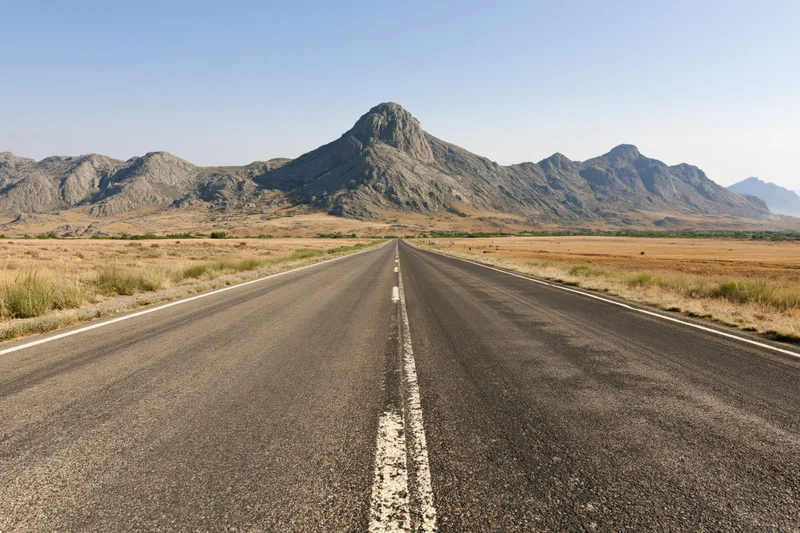 Straight asphalt highway stretching through arid desert landscape toward distant mountains under clear blue sky