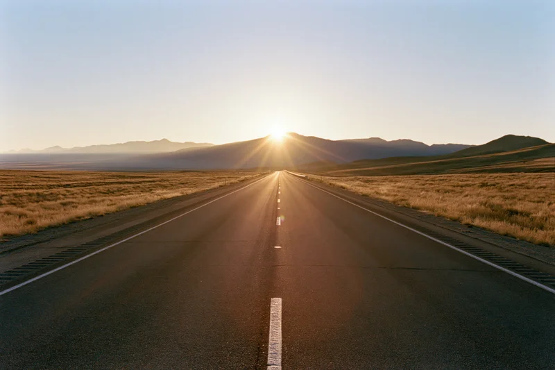Straight asphalt highway stretching toward distant mountains at sunset over open desert landscape