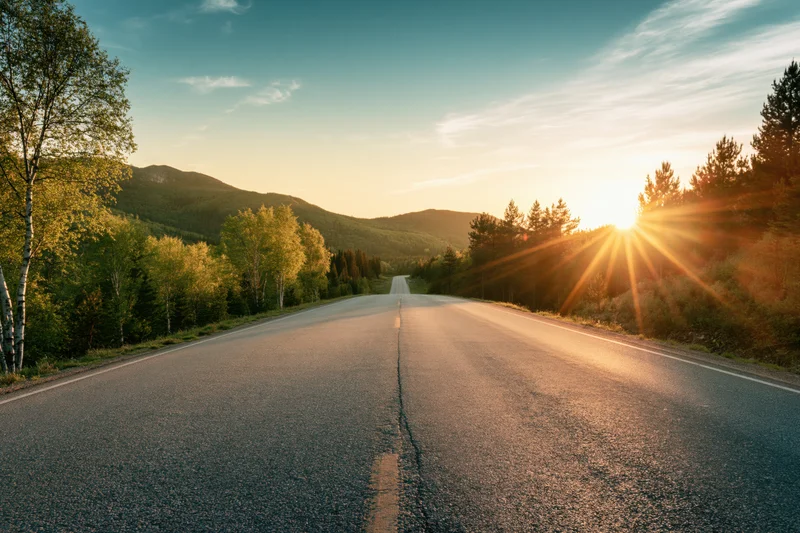 Straight asphalt highway stretching into the distance through forested mountains at sunset